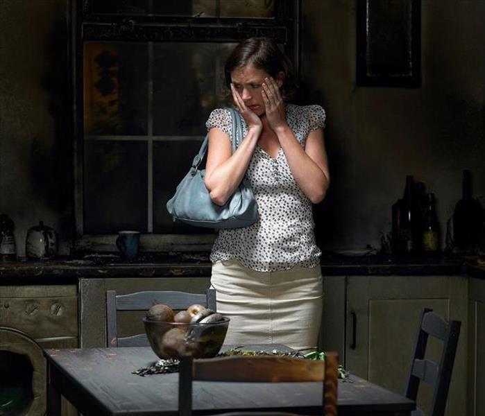 A picture of a women in shock standing in her kitchen after a fire. 