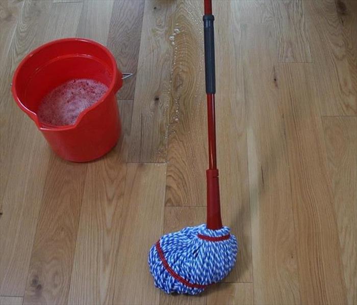 A picture of light brown hardwood flooring with a mop and a full bucket of mop water. 